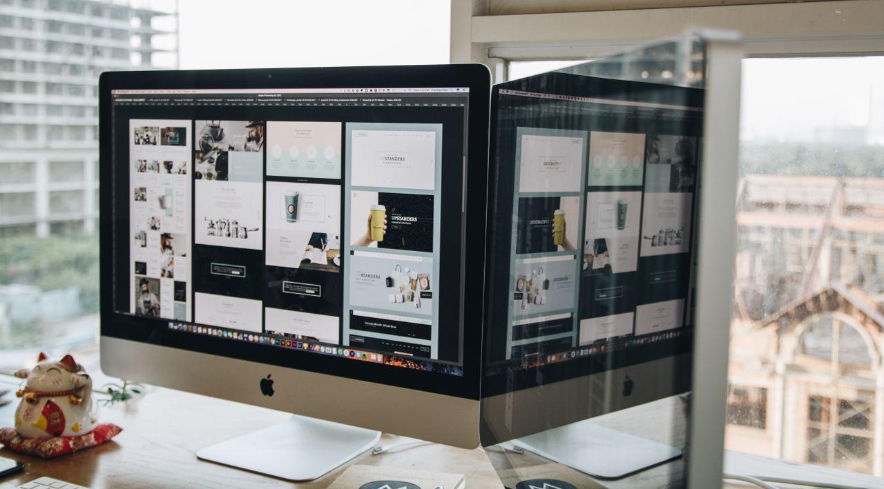 team-03 Dual monitors on a desk, showcasing web design in a modern office setting.